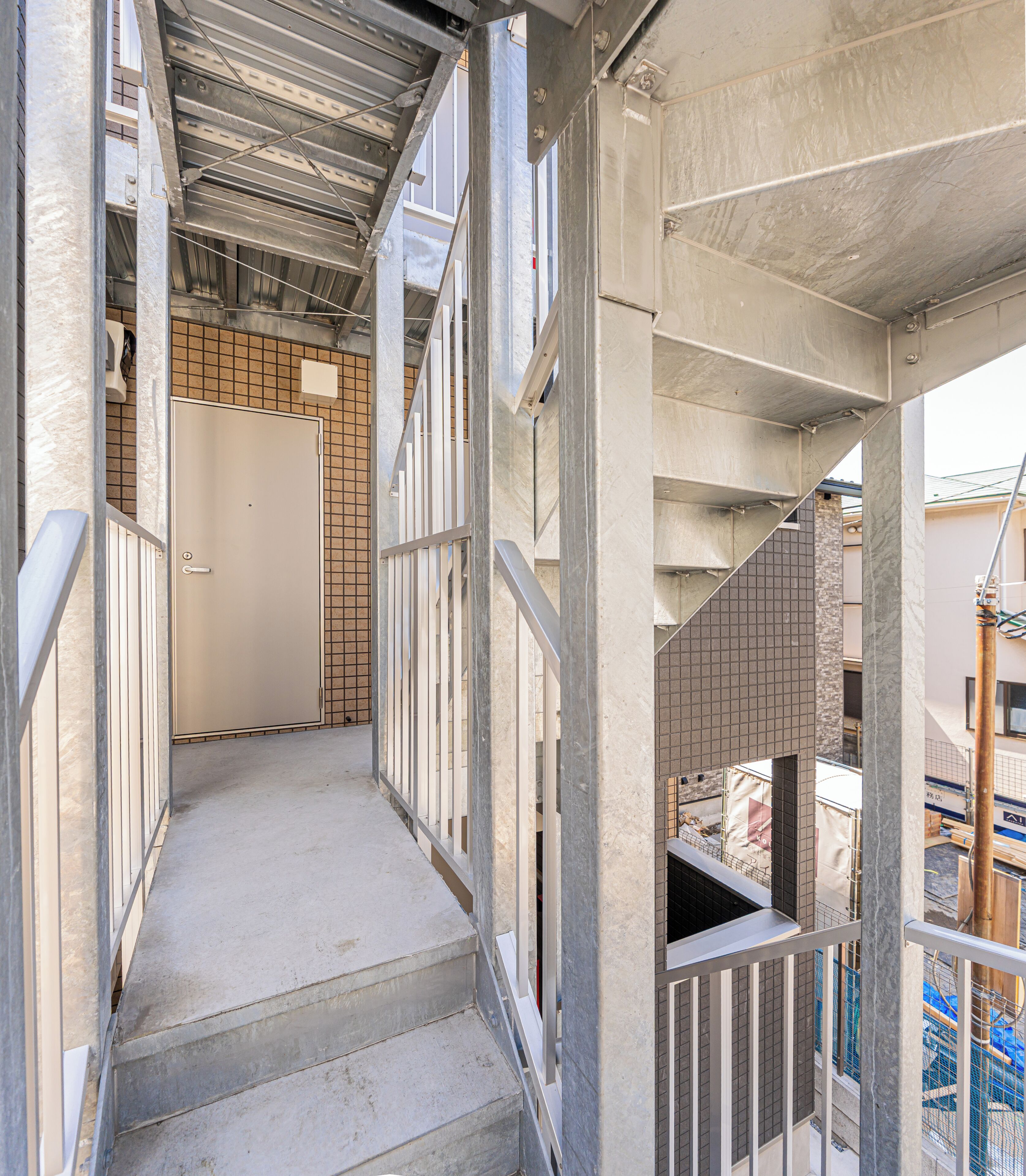 A narrow corridor with metal railings, a concrete floor, and a door at the end.