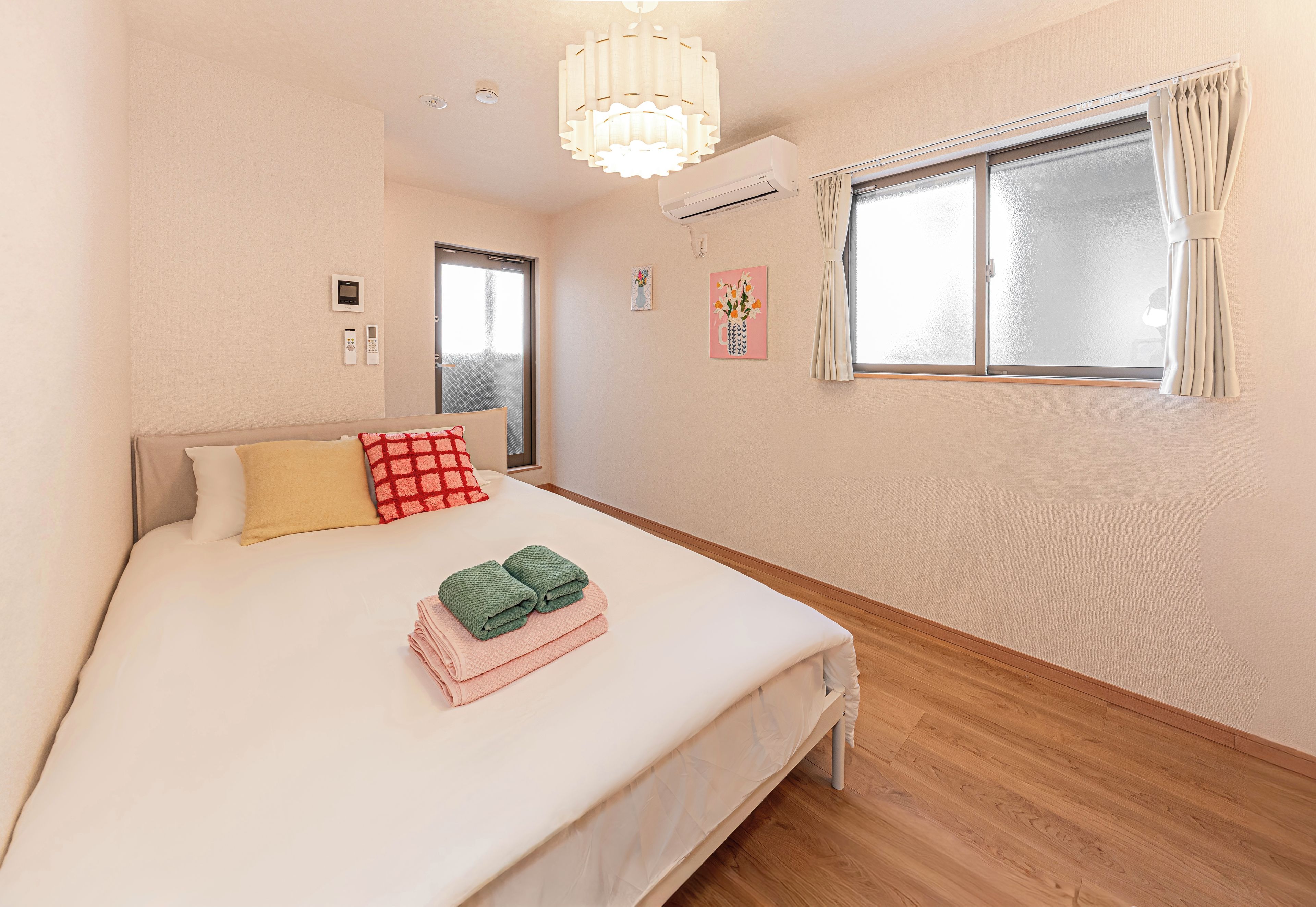 Une chambre à coucher avec un lit, une fenêtre avec des rideaux, un climatiseur fixé au mur et un luminaire au plafond.