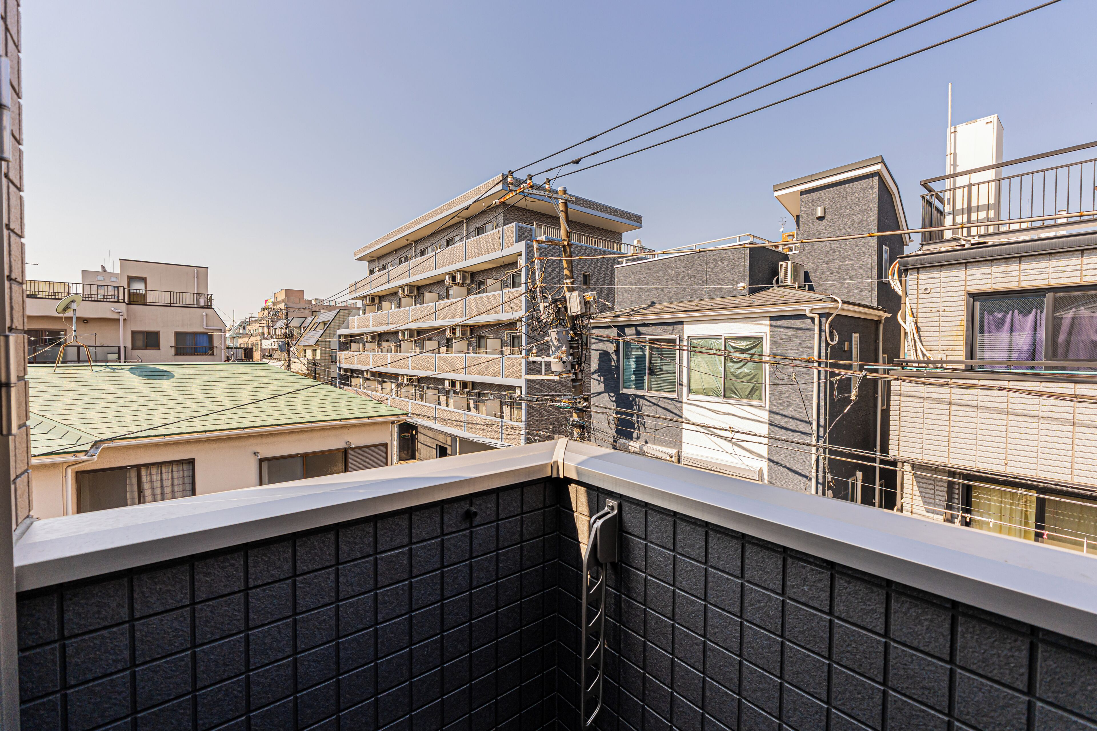A multi-story residential building with balconies, visible power lines, and a clear sky.