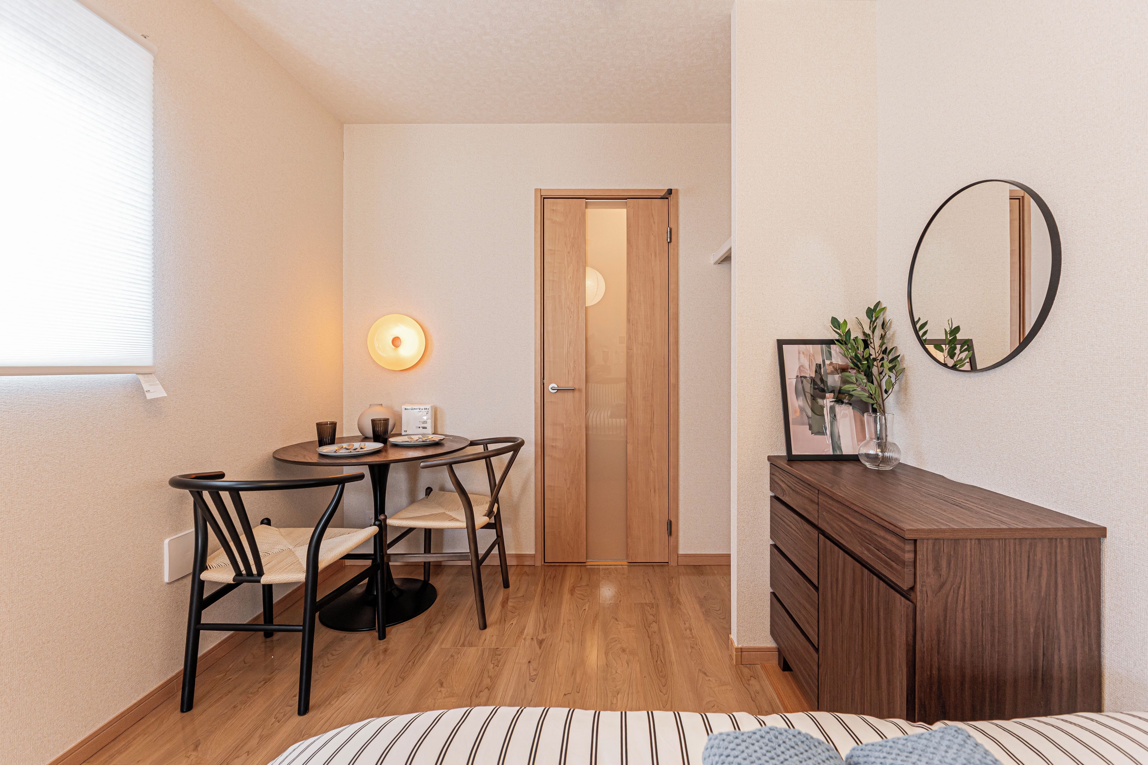 Een kleine kamer met een eettafel, stoelen, een houten kledingkast, een spiegel en een deur.