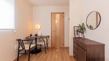 Een kleine kamer met een eettafel, stoelen, een houten kledingkast, een spiegel en een deur.