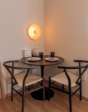 Uma mesa de jantar redonda com duas cadeiras, uma luminária na parede e um abajur.