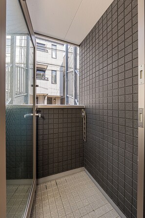 A small, enclosed bathroom with a tiled floor and walls, a glass door leading outside, and a window providing a view of the outside. - The Parknest Haneda (Tokyo)