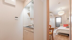 A modern hotel room with a kitchenette, a bed with a red pillow, and a large window. - The Parknest Haneda (Tokyo)