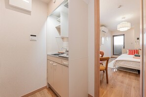 Quarto de hotel moderno com cozinha compacta, cama com travesseiro vermelho e uma janela grande.
