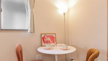 A corner room with a round table, two chairs, a window with curtains, a floor lamp, and a framed picture on the wall.