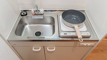 A kitchen with a stainless steel sink, a stove with a pot, and a cabinet below.