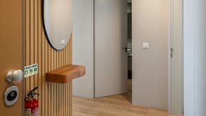 Een gang met een houten paneelwand, een ronde spiegel, een houten plank en een brandblusser, met een deur die naar een badkamer leidt.