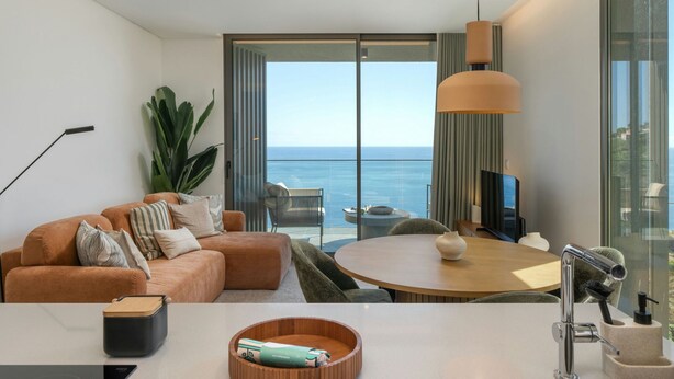 Een moderne woonkamer met een bank, een eettafel en uitzicht op zee.