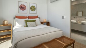 Een moderne slaapkamer met een groot bed, een nachtkastje met lamp, en een badkamer zichtbaar door een geopende deur.