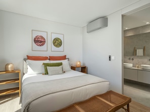 A modern bedroom with a large bed, a bedside table with a lamp, and a bathroom visible through an open door. - Azure Calheta by Interhome (Calheta (Madeira))