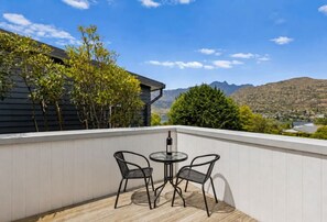 A balcony with a table and chairs, overlooking a mountainous landscape. - Spacious 3 BDRM, Panoramic Views and 2 Carparks! (Queenstown)
