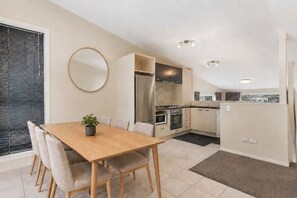 A modern kitchen with a dining area, including a wooden table and chairs, a potted plant, and built-in appliances. - Spacious 3 BDRM, Panoramic Views and 2 Carparks! (Queenstown)