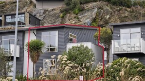 Et moderne hus med balkon, omgivet af vegetation og en klippeskråning.