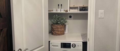 A laundry room with a washing machine, shelves with baskets, and a small plant.