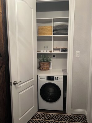 A laundry room with a washing machine, shelves with baskets, and a small plant. -     Business & Family Friendly Casita (Katy)