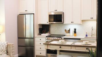 A modern kitchen with white cabinets, stainless steel appliances, and a dining area with a wooden table and chairs.