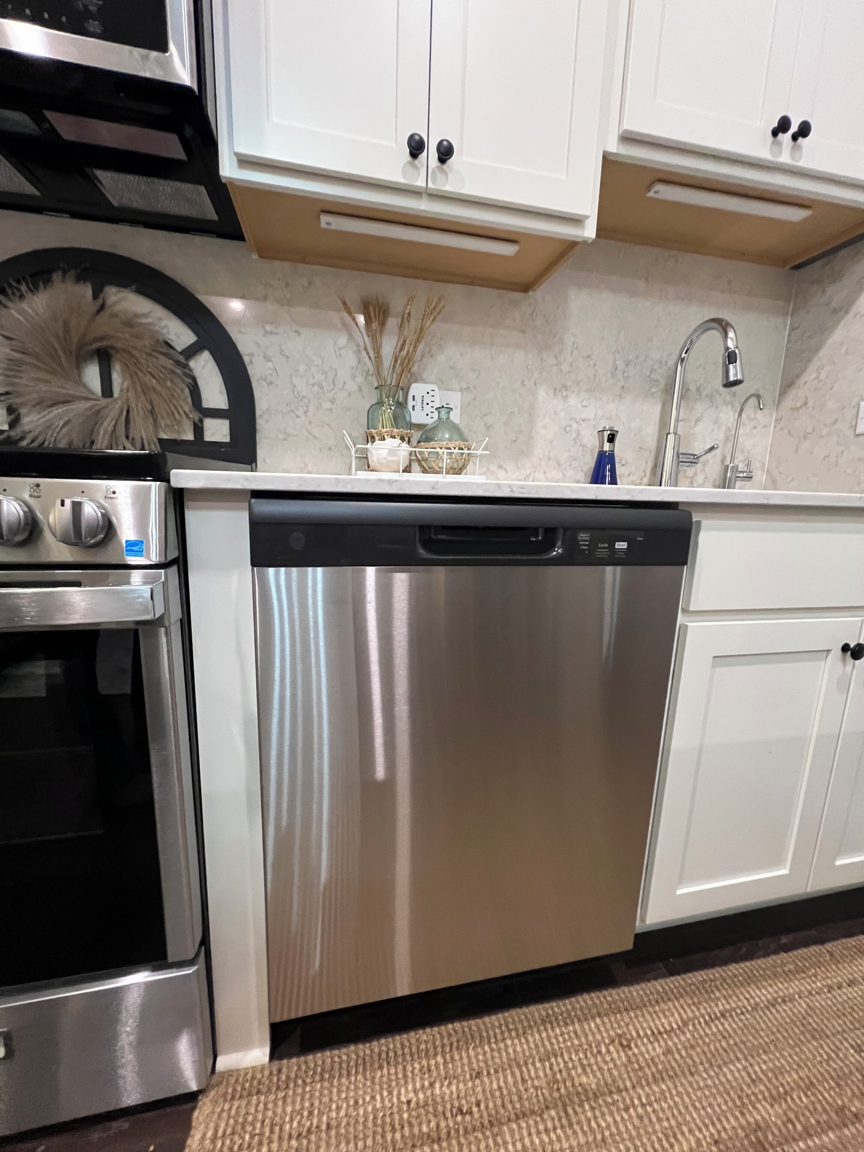 A kitchen with stainless steel appliances, white cabinets, and a marble countertop.