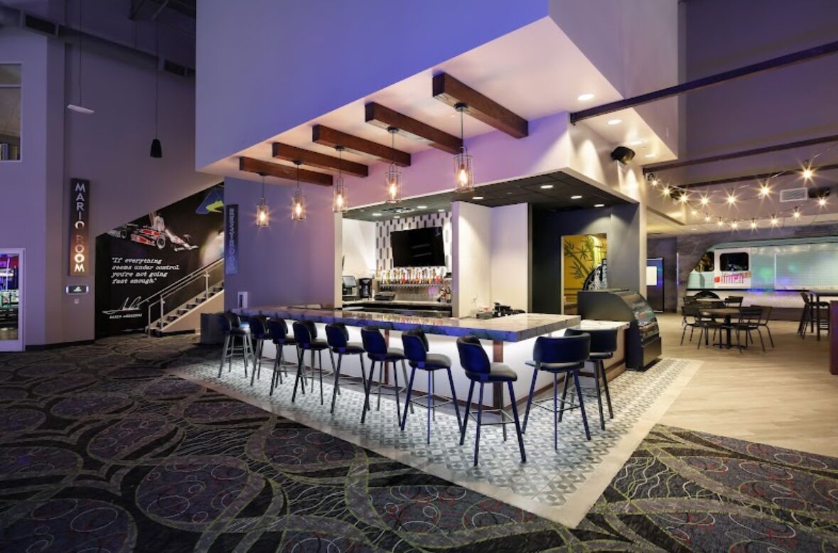 A modern bar area with a long counter, bar stools, and a television screen.
