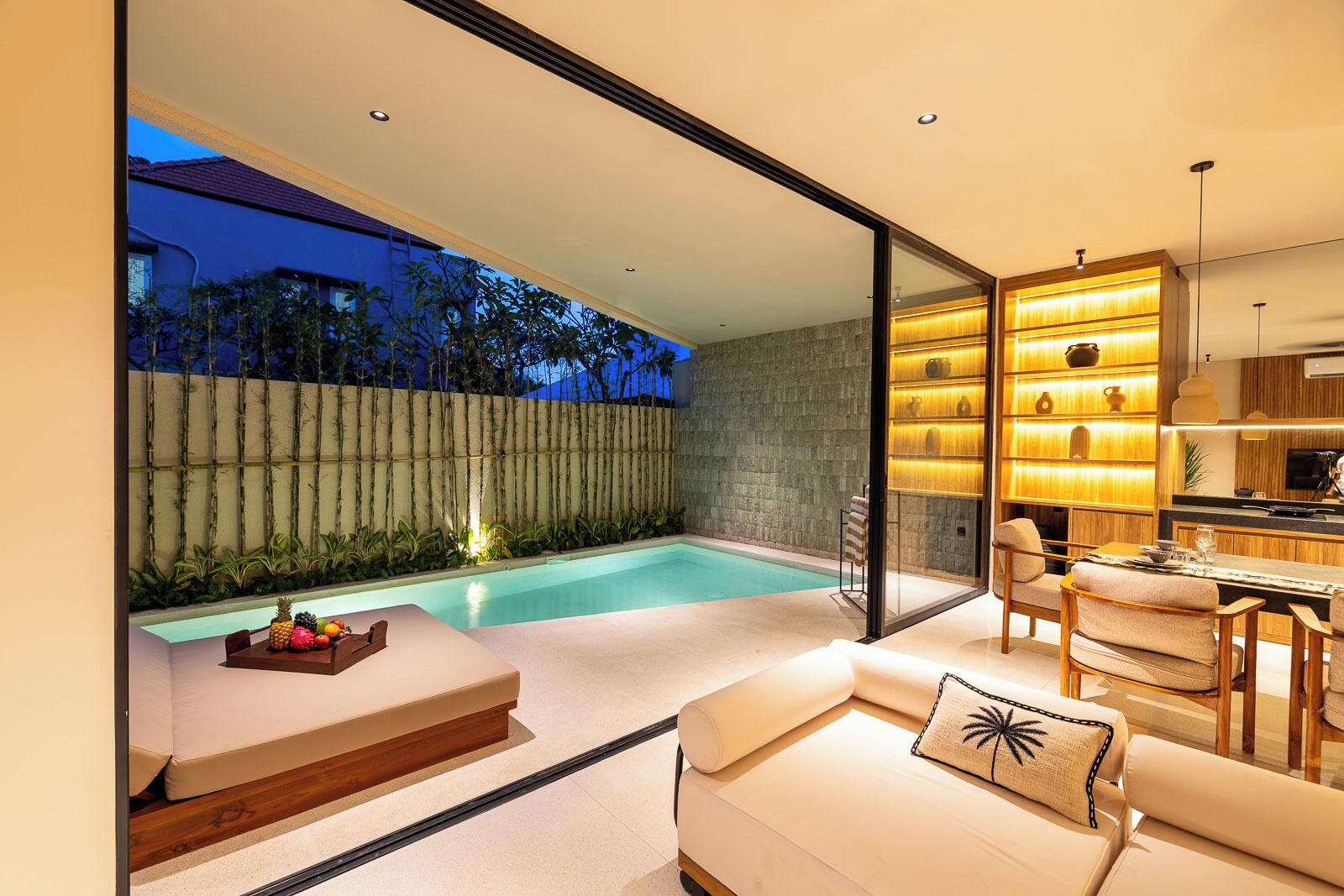 A modern outdoor living space with a pool, seating area, and a kitchen with illuminated shelves.