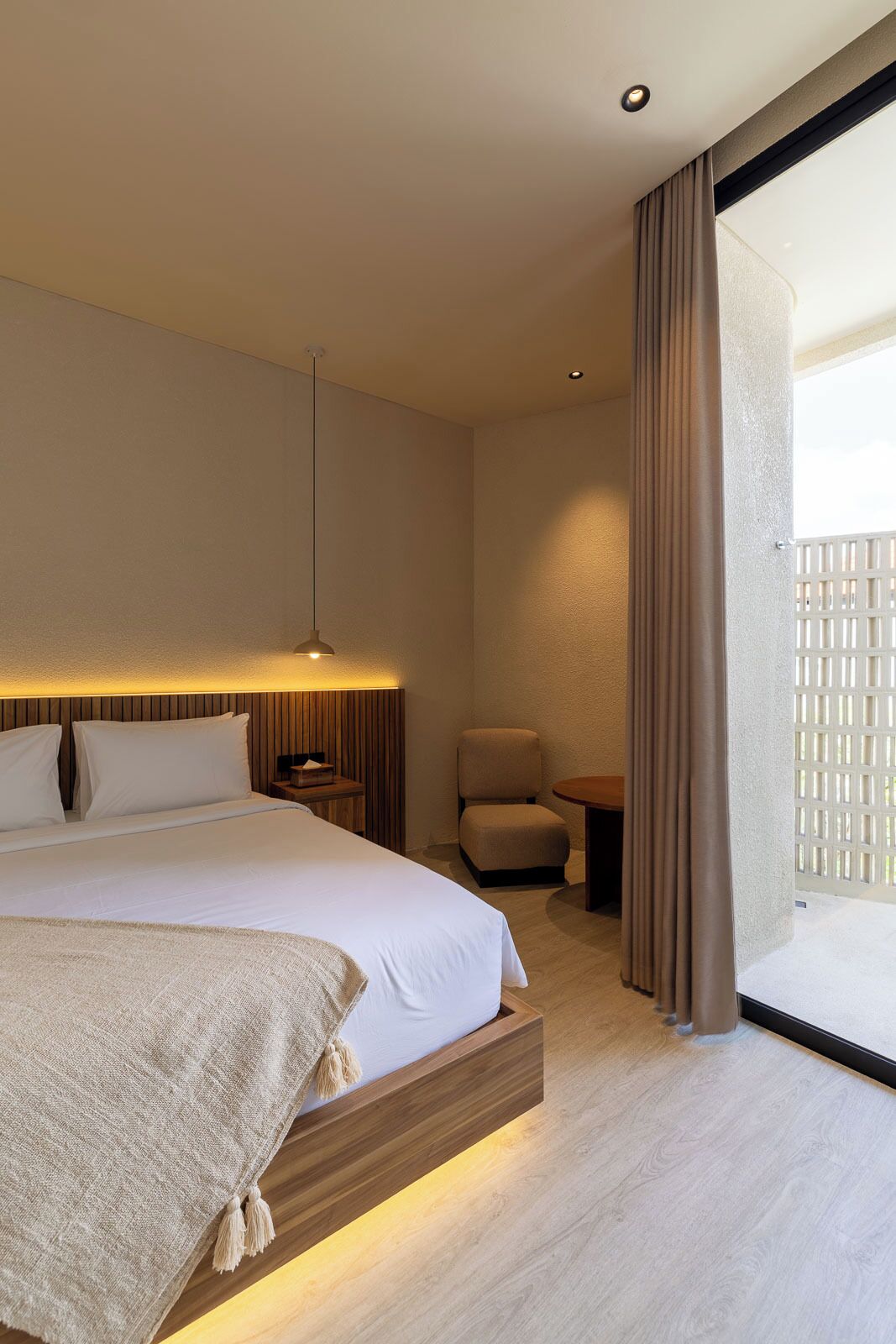 A hotel room with a bed, bedside table, chair, and a view of the outside.