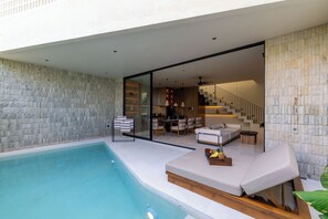 Un espacio exterior moderno con piscina, zona de estar con sofá y mesa, y una escalera que conduce a un nivel superior.
