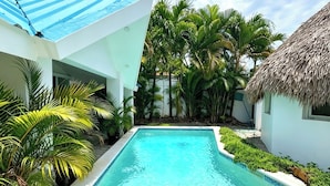 A swimming pool with clear blue water, surrounded by tropical plants and a thatched-roof structure. - Bungalow with a pool, just a few minutes from the beaches (Las Terrenas)