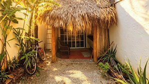 A thatched-roof structure with a gravel pathway leading to a door, surrounded by tropical plants and a bicycle. - Bungalow with a pool, just a few minutes from the beaches (Las Terrenas)