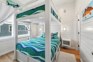 A bunk bed room with a striped blue and green bedspread, white walls, and a window with blinds.