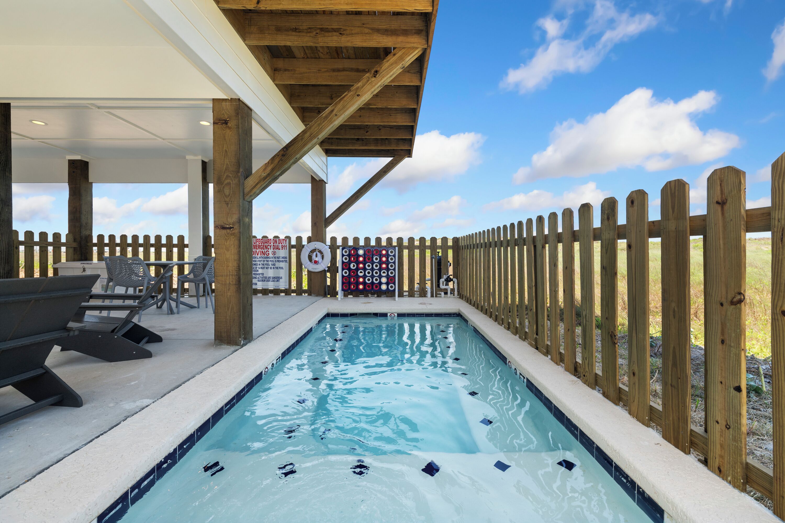 Un espace piscine doté d’une terrasse en bois, de chaises longues et d’un panneau indiquant la présence d’un sauveteur.