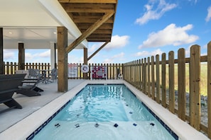 A pool area with a wooden deck, lounge chairs, and a lifeguard on duty sign.