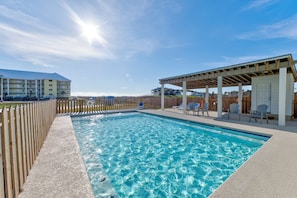 Une piscine avec une terrasse en bois, des chaises longues et un espace salon abrité.