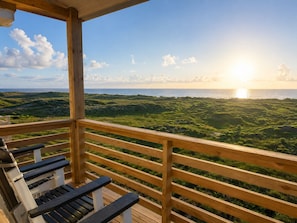 A wooden deck with a view of the ocean and grassy landscape.