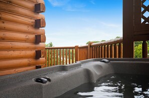 Ein Whirlpool auf einer Holzterrasse mit Blick auf einen See und Bäume.