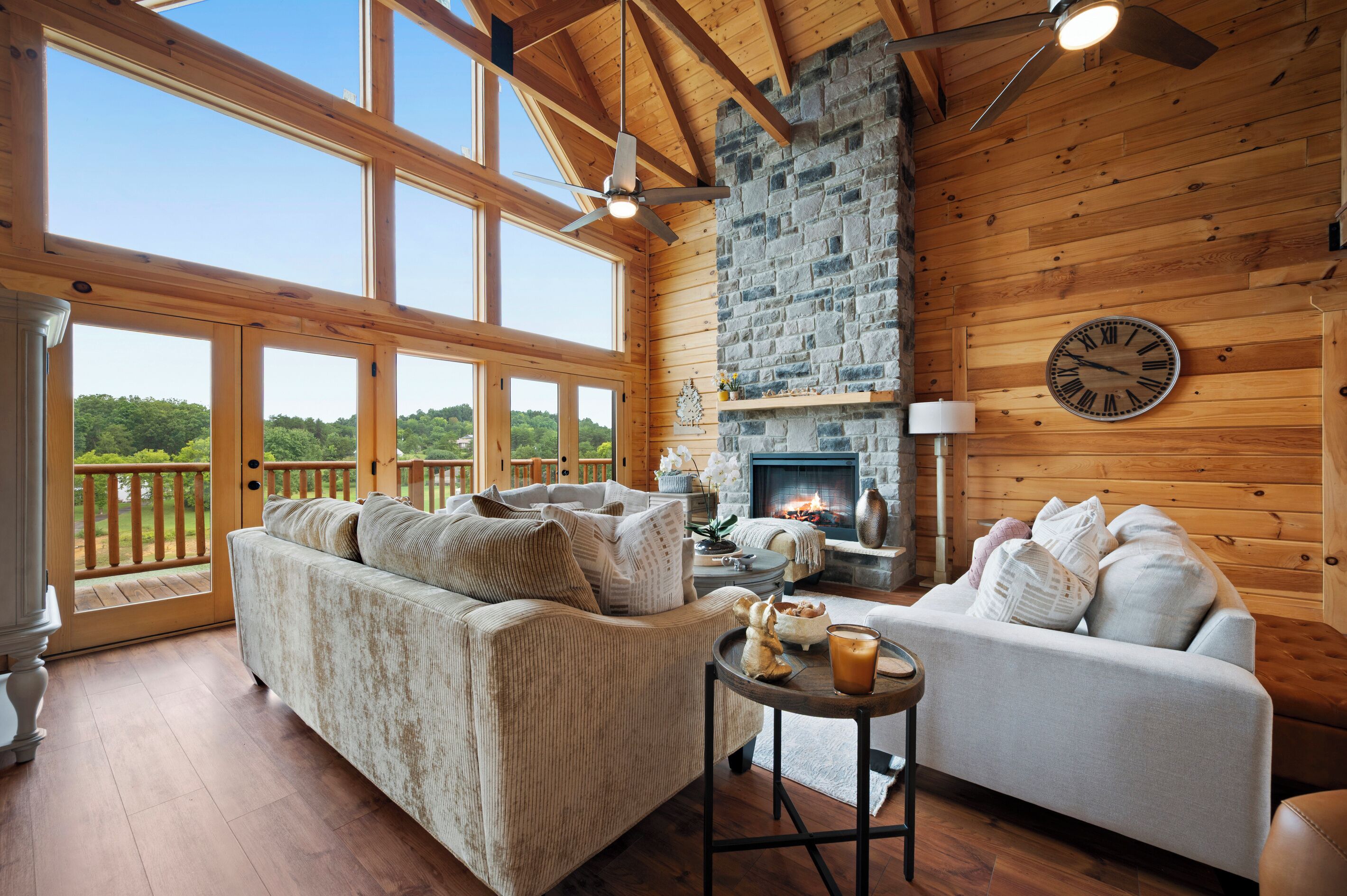 A cozy living room with a fireplace, wooden walls, and large windows overlooking a forest.