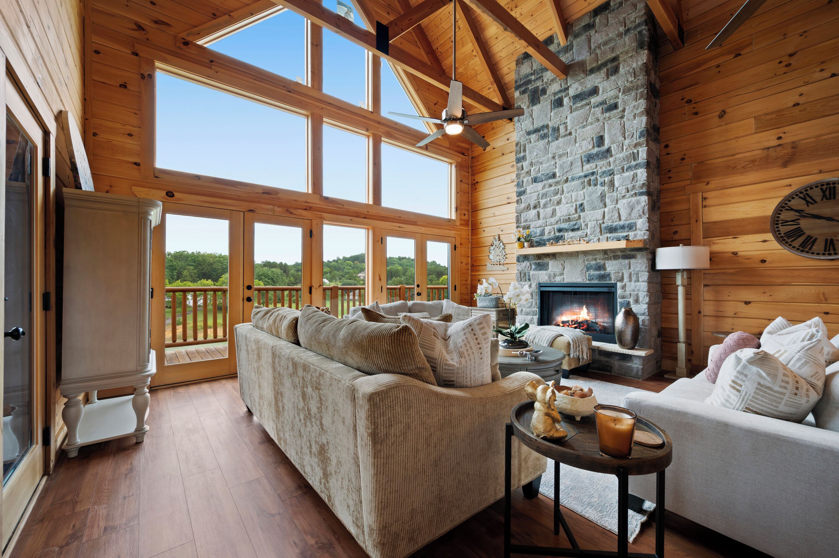 A cozy cabin interior with a large window, a stone fireplace, and a wooden ceiling.