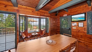 Ein Holzblock-Interieur mit einem Esstisch, Stühlen, einem Fernseher und Blick ins Freie.