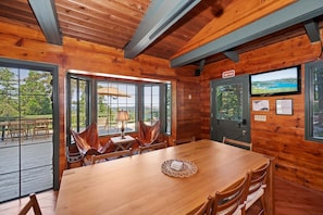 Ein Holzblock-Interieur mit einem Esstisch, Stühlen, einem Fernseher und Blick ins Freie.