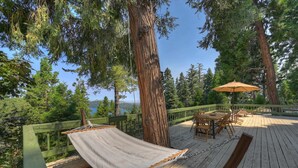 Eine Holzterrasse mit einer Hängematte, Gartenmöbeln und Blick auf einen von Bäumen umgebenen See.
