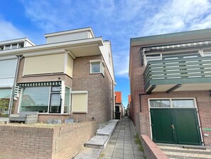 A narrow alleyway between two brick buildings with a green door and a window with shutters. - SunnyLogde by Interhome (Noordwijk)