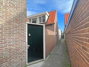 A narrow alleyway between brick buildings with a door and a window on the left. - SunnyLogde by Interhome (Noordwijk)