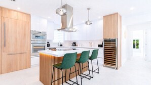 A modern kitchen with a central island, bar stools, stainless steel appliances, and pendant lighting. - Designer Pool Home • Near Las Olas • Sleeps 10 (Fort Lauderdale)
