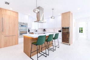 A modern kitchen with a central island, bar stools, stainless steel appliances, and pendant lighting. - Designer Pool Home • Near Las Olas • Sleeps 10 (Fort Lauderdale)