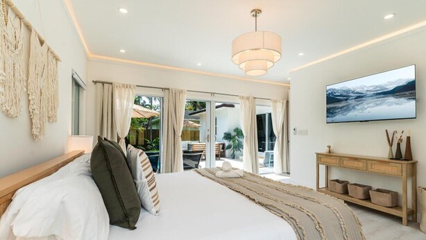 A bedroom with a large bed, a TV, a wooden console, and a view of the outdoors. - Designer Pool Home • Near Las Olas • Sleeps 10 (Fort Lauderdale)