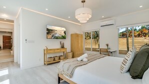 A modern bedroom with a large bed, a wooden console table, a TV on the wall, and a view of the outdoors through a sliding door. - Designer Pool Home • Near Las Olas • Sleeps 10 (Fort Lauderdale)