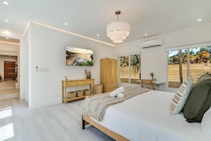 A modern bedroom with a large bed, a wooden console table, a TV on the wall, and a view of the outdoors through a sliding door. - Designer Pool Home • Near Las Olas • Sleeps 10 (Fort Lauderdale)