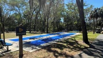 A pool area with a shuffleboard table, surrounded by trees and shaded by large branches.