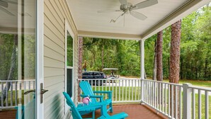 Eine überdachte Veranda mit Deckenventilator, Holzterrasse und türkisblauen Adirondack-Stühlen.