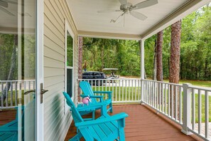 Eine überdachte Veranda mit Deckenventilator, Holzterrasse und türkisblauen Adirondack-Stühlen.