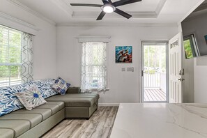 A room with a sectional sofa, a ceiling fan, a painting, and a door leading to an outdoor area. - New Crystal River Resort Cabin w/Pool & Boat Prkng (Crystal River)